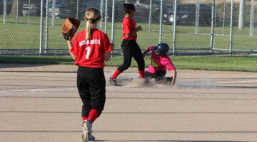 A girls softball player watches a play unfold at third base