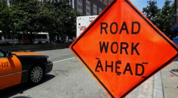 An orange "road work ahead" sign on a city street