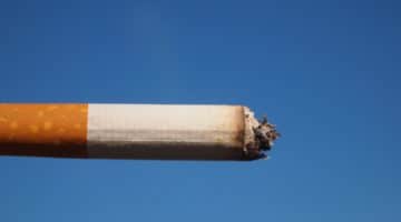 A burning cigarette pictured against a clear, blue sky