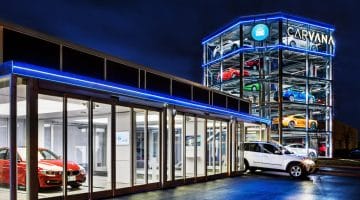 An illustration of a Carvana dealership at night, with a "vending machine" tower filled with cars