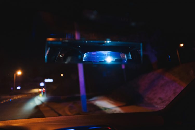 A police SUV visible in the rearview mirror of a driver pulled over for speeding